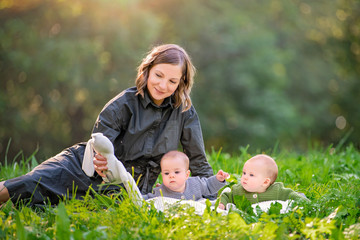 happy mom sits in the park on the grass with twins babies, smiling