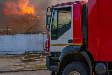 Flame and black smoke from a burning building. Fire truck. Firefighting.