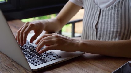 Close up of woman's hands typing on laptop. Woman working on laptop  while sitting at table in cozy cafeteria