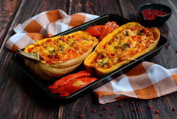 Dark baking tray with baked pumpkin and halves of pepper and a checkered towel