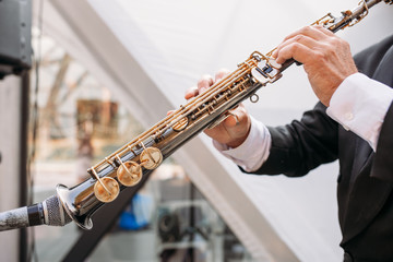 A musician at the event in a frock coat and bow tie plays the saxophone. Сlose-up of hands and...