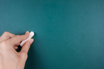 Naklejka premium woman's left hand holds a white chalk and is about to write on a green Board, copying space.