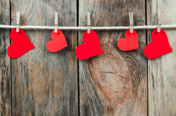 Red paper hearts hang on a clothesline with clothespins on a wooden background, copying the space. Beautiful, festive background