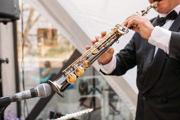 A musician at the event in a frock coat and bow tie plays the saxophone. Сlose-up of hands and...