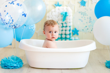 baby boy celebrates birthday 1 year in a bath with balloons, bathing baby with blue balloons