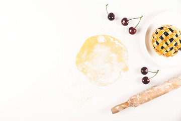 Kitchen white table - the process of making an autumn mini cake with cherries among dough, eggs and flour. Top view with copy space