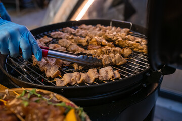 Catering banquet outdoors. A chef with gloves prepares barbecue on skewers. Hands and meat close up