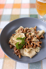 Papardelle pasta with wild foraged chanterelle mushrooms in a creamy white wine sauce in a grey bowl on a table cloth
