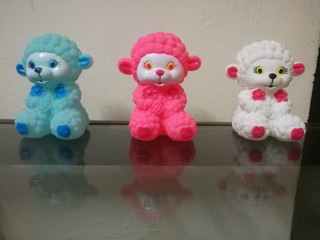 Three sheep dolls of different colors placed in a line and their reflections on the glass.