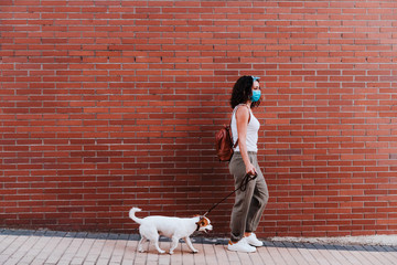 young woman walking outdoors wearing protective mask, cute jack russell dog besides. New normal...