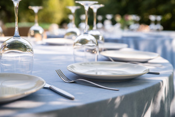 Served tables for a banquet or wedding in the summer outdoors. Tables with a blue tablecloth, white...