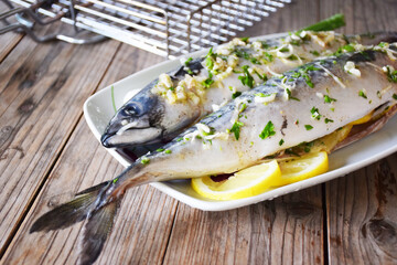 marinated fish on a plate with lemon and olives on a textured wooden background, near the grill. tasty and healthy food