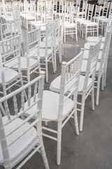 Empty white chairs for guests at a banquet or wedding on an outdoor summer area are in a row