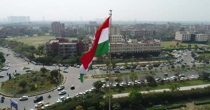 Wide-angle & fast-rotating Drone shot of the Indian Tricolour Flag Fluttering over a commercial area of Gurugram Metropolitan City in North India