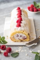 Sponge cake roll filling cream and raspberries, on white stone background. Soft focus. Summer food concept
