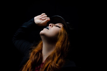 Portrait of a beautiful redhead with hat made in studio, low key image, with black background.