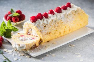 Sponge cake roll filling cream and raspberries, on white stone background. Soft focus. Summer food concept