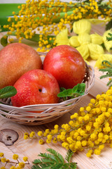 Plums and pears in a wicker basket on the wooden table. Spring still life