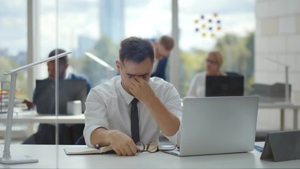 Tired young businessman feeling stressed and taking off eyeglasses having eye strain