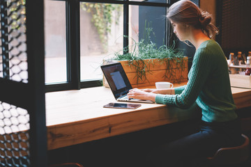 Talented female student dressed in casual outfit making presentation for coursework project on laptop computer.Skilled IT developer working on freelance and coding program sitting at table in cafe