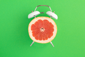 Half a grapefruit on the dial of the alarm clock in the center of the green surface