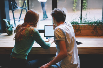 Back view of male and female students dressed casual outfit browsing useful information on websites while making coursework presentation via laptop connected to wireless internet in coworking space