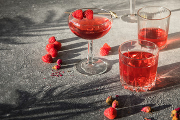 Smash gin alcoholic cocktail. Long raspberry drink on  gray stone background, copy space. Sunlight...