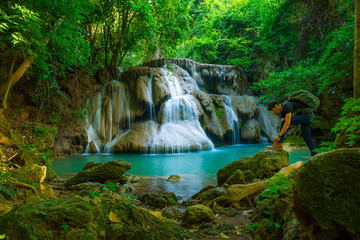 Naklejka premium PhotosSearch by image Young man with backpack standing near a waterfall in forest. Male hiker in the nature during rain