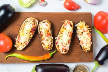preparation homemade stuffed eggplant in the shape of a boat with baked vegetables and mozzarella cheese, ingredients tomatoes, peppers, onions, eggplant . on a light background top view