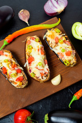preparation homemade stuffed eggplant with vegetables and mozzarella cheese, ingredients tomatoes, peppers, onions, eggplant . on a dark background top view