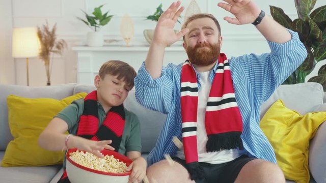 Excited caucasian father and son wathing TV waiting for match ending. Unhappy young family of football fans losing the game frutrating. Soccer games. Home entertainment.