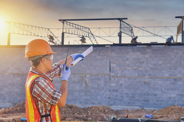 Construction engineers supervising progress of construction project stand on new factory,Engineering Consulting People on construction site holding blueprint in his hand.