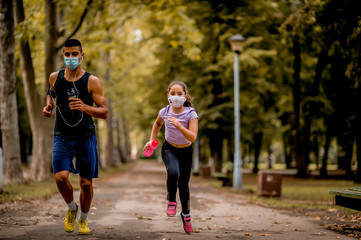 Young sporty man and girl are running in the park. They are wearing a protective face mask