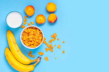 Breakfast cereals, bananas, apricots and a glass of milk on a bright blue background top view, flat lay. Fitness food concept. Breakfast with cornflakes, milk and fruit. Copy space.