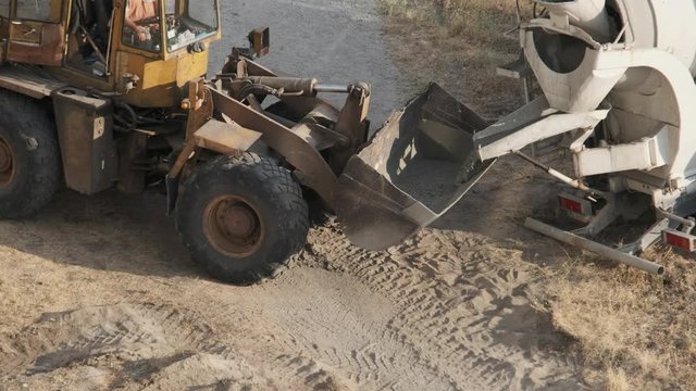 Concrete Mixer Fills Bulldozer Bucket with Liquid Concrete at Construction Site