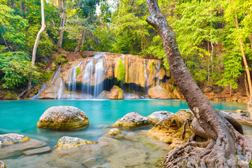 Tropical landscape with beautiful waterfall, emerald lake, rocks and large tree roots in wild jungle forest. Erawan National park, Kanchanaburi, Thailand