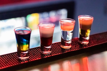 Short drinks at night bar. Four glasses of alcoholic cocktails. Colorful neon light, dark shadows.