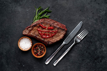 grilled beef steak with spices, knife and fork for halloween on stone background