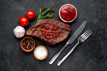 grilled beef steak with spices, knife and fork for halloween on stone background