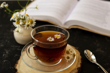 English tea with chamomile stands on a wooden frame and a teaspoon and an open book for reading...