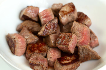 seared meat in a bowl on white background