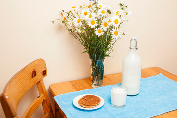 Simply stylish wooden kitchen with bottle of milk and glass on table, summer flowers camomile, healthy foog moring concept