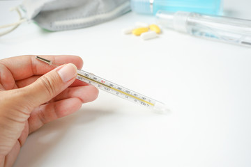 Hand holding mercury thermometer showing high temperature or have a fever with personal protective...