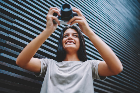 Happy smiling female amatour photographer 20 years old checking photos on vintage camera and recalls pleasant moments while waiting friend outdoors, retro and old fashioned technology concept