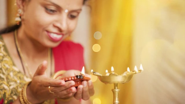 Selective focus on hands, Happy smiling Indian woman lighting lantern or Diya Lamp during festival ceremony at home - concept of traditional festival and ritual celebrations.