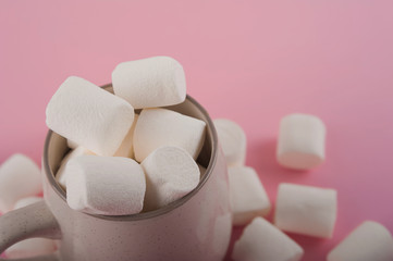 Marshmallows in a mug on a pink background close-up and copy space. Marshmallow in cocoa or hot chocolate top view on a pink background.