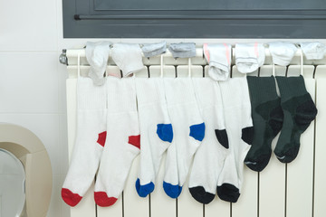 Coloured socks drying on the heating radiator next to the washing machine with the entrance open. Concept of housework.