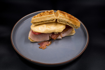 Sandwich de waffle con jamón y tocino sobre fondo negro 