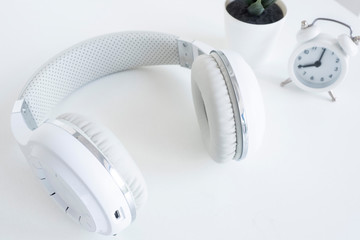 white wireless headphones and a small white alarm clock on a white table..