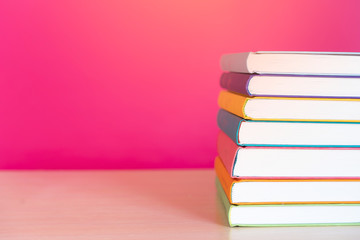 Stack of colorful books, bright colorful pink background, free copy space. Books on table, no labels, blank spine. Back to school. Education background